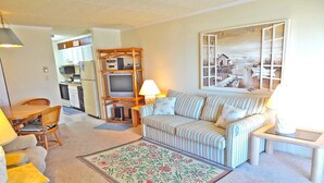 A living room with a sofa, a TV, and a dining area with chairs and a table. - Barefoot Country 304-Oceanfront 138th St, WIFI, Elev, W/D, AC (Ocean City)