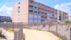 A multi-story building with balconies, a sandy path, and a wooden fence. - Barefoot Country 304-Oceanfront 138th St, WIFI, Elev, W/D, AC (Ocean City)