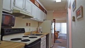 A compact kitchen with white cabinets, a microwave, stove, and refrigerator. - Barefoot Country 304-Oceanfront 138th St, WIFI, Elev, W/D, AC (Ocean City)