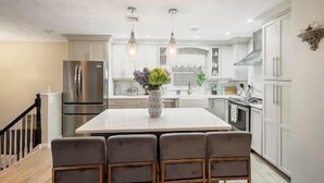 Une cuisine moderne dotée d’un îlot central, d’appareils électroménagers en acier inoxydable et de luminaires suspendus.