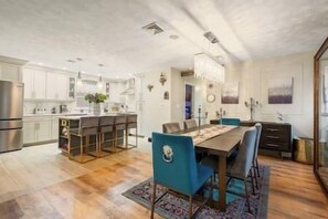 Une cuisine spacieuse avec des meubles blancs, un îlot central et un coin repas comprenant une grande table et des chaises bleues.
