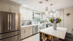 Une cuisine moderne dotée d’appareils électroménagers en acier inoxydable, de meubles blancs et d’un îlot central agrémenté d’un vase de fleurs.