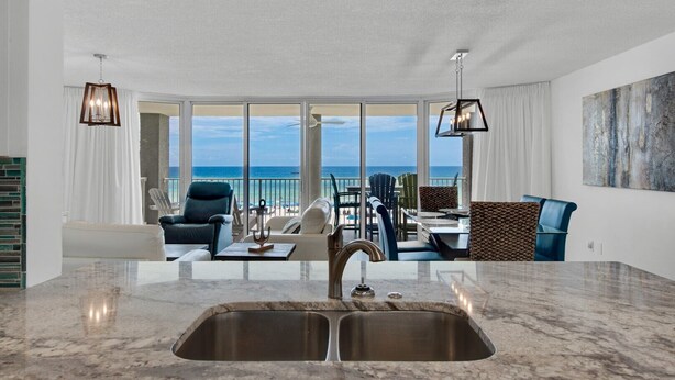 A modern kitchen with a large island, a dining area with chairs and a table, and a view of the ocean through large windows.
