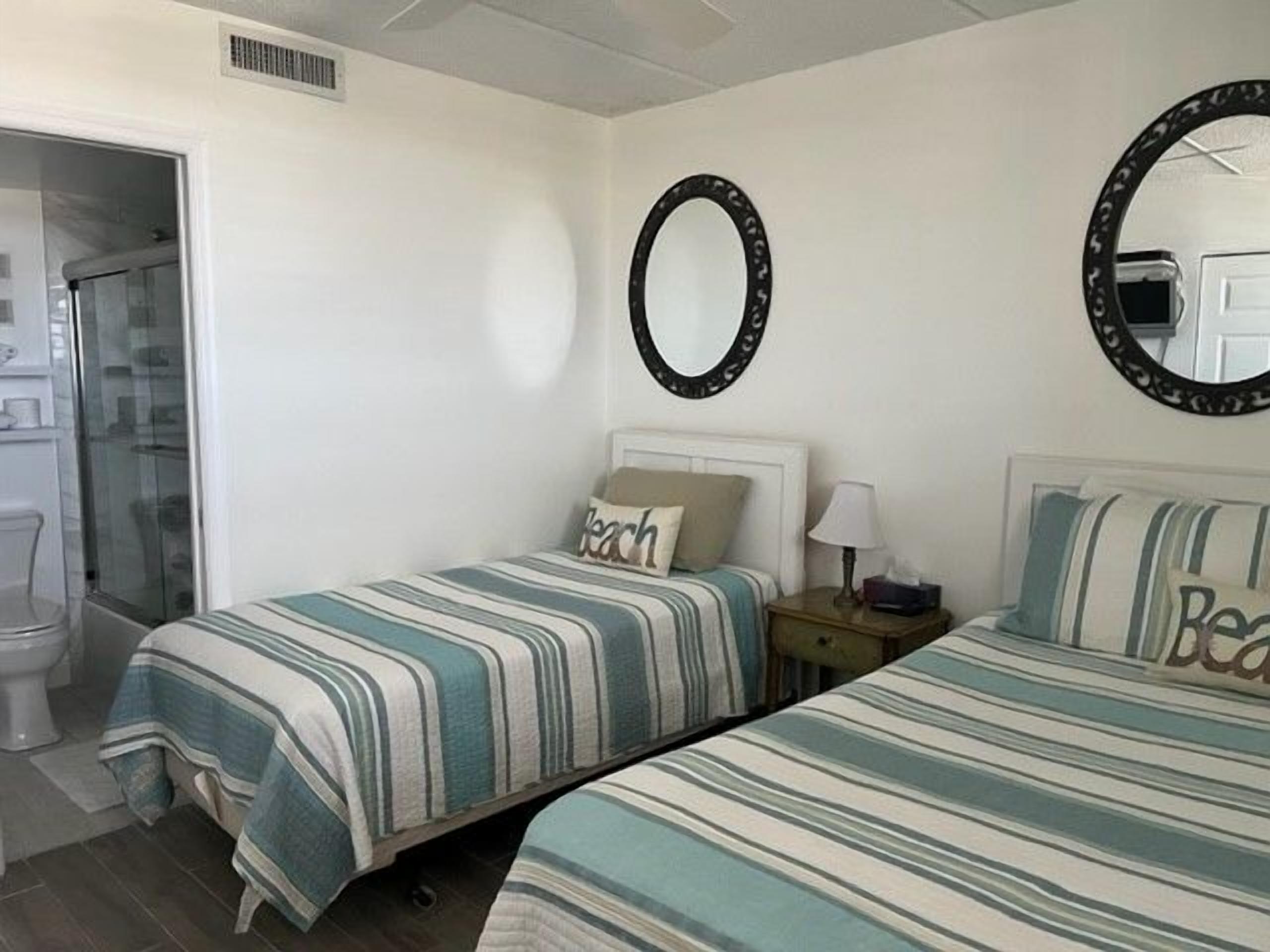 Un dormitorio con dos camas, un espejo y una mesita de noche con lámpara.
