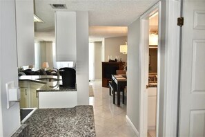 A modern kitchen with granite countertops, a dining area with a table and chairs, and a visible hallway leading to other rooms. - Perfect Location in Ponce Inlet for this 2/2 oceanfront Condo 504 South Point (Ponce Inlet)