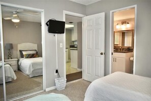 A hotel room with a bed, a mirror, a television, and a bathroom with a sink and mirror.
