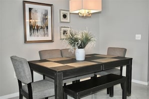 A dining table with a vase of plants, grey upholstered chairs, and a framed picture on the wall.