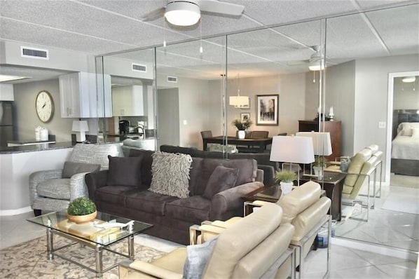 A modern living room with a sofa, armchairs, a coffee table, and a dining area with a table and chairs.