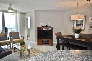 A modern living room with a flat-screen TV, comfortable seating, a dining table, and a large window offering a view. - Perfect Location in Ponce Inlet for this 2/2 oceanfront Condo 504 South Point (Ponce Inlet)
