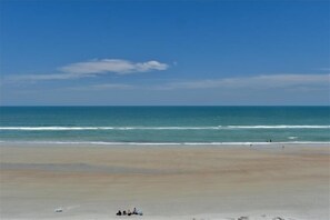 A beach with a clear sky, calm sea, and a few people in the distance.