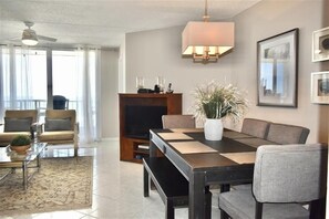 A modern living room with a dining table, chairs, a television, and a ceiling fan. - #504 Southpoint 2/2 Oceanfront Traffic Free Beach (Ponce Inlet)