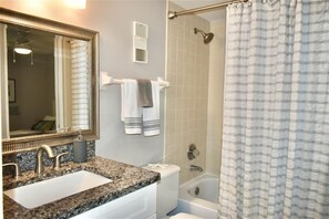 A bathroom with a granite countertop sink, a large mirror, a towel rack with towels, a shower curtain, and a bathtub. - Perfect Location in Ponce Inlet for this 2/2 oceanfront Condo 504 South Point (Ponce Inlet)