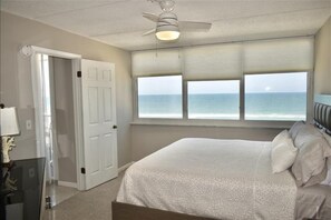 A bedroom with a bed, a ceiling fan, a window with a view of the ocean, and a door. - Perfect Location in Ponce Inlet for this 2/2 oceanfront Condo 504 South Point (Ponce Inlet)