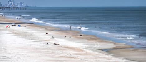 A beach with a pier in the background, sandy shore, and a few people.