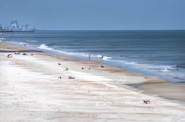 A beach with a pier in the background, sandy shore, and a few people.