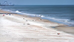 Une plage avec une jetée en arrière-plan, un rivage sablonneux et quelques personnes.