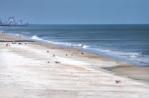 A beach with a pier in the background, sandy shore, and a few people. - 7th Floor Unit 709 Oceanfront with Great Views in Ponce Inlet (Ponce Inlet)