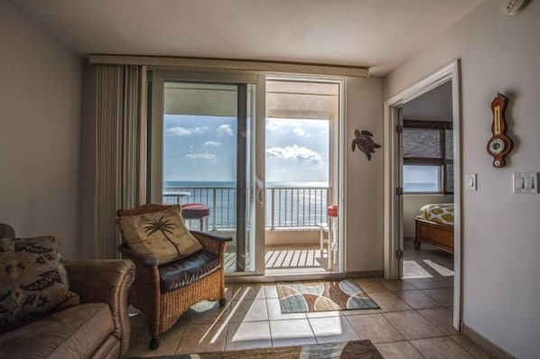 A room with a balcony, a wicker chair, a sofa, and a bed.