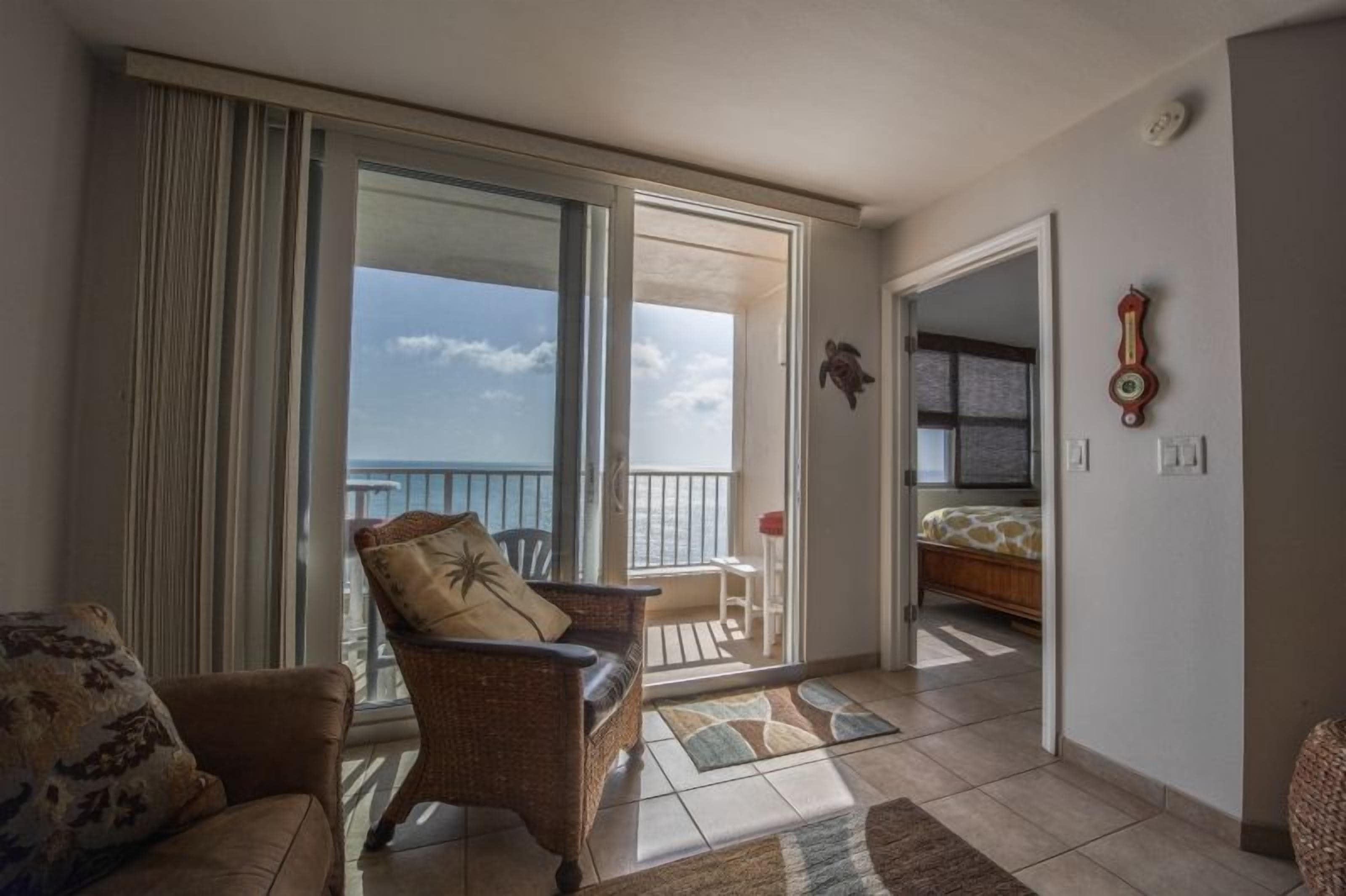 Een kamer met balkon, een rieten stoel, een tafeltje en een bed.