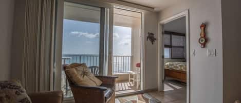 A room with a balcony, a wicker chair, a small table, and a bed.