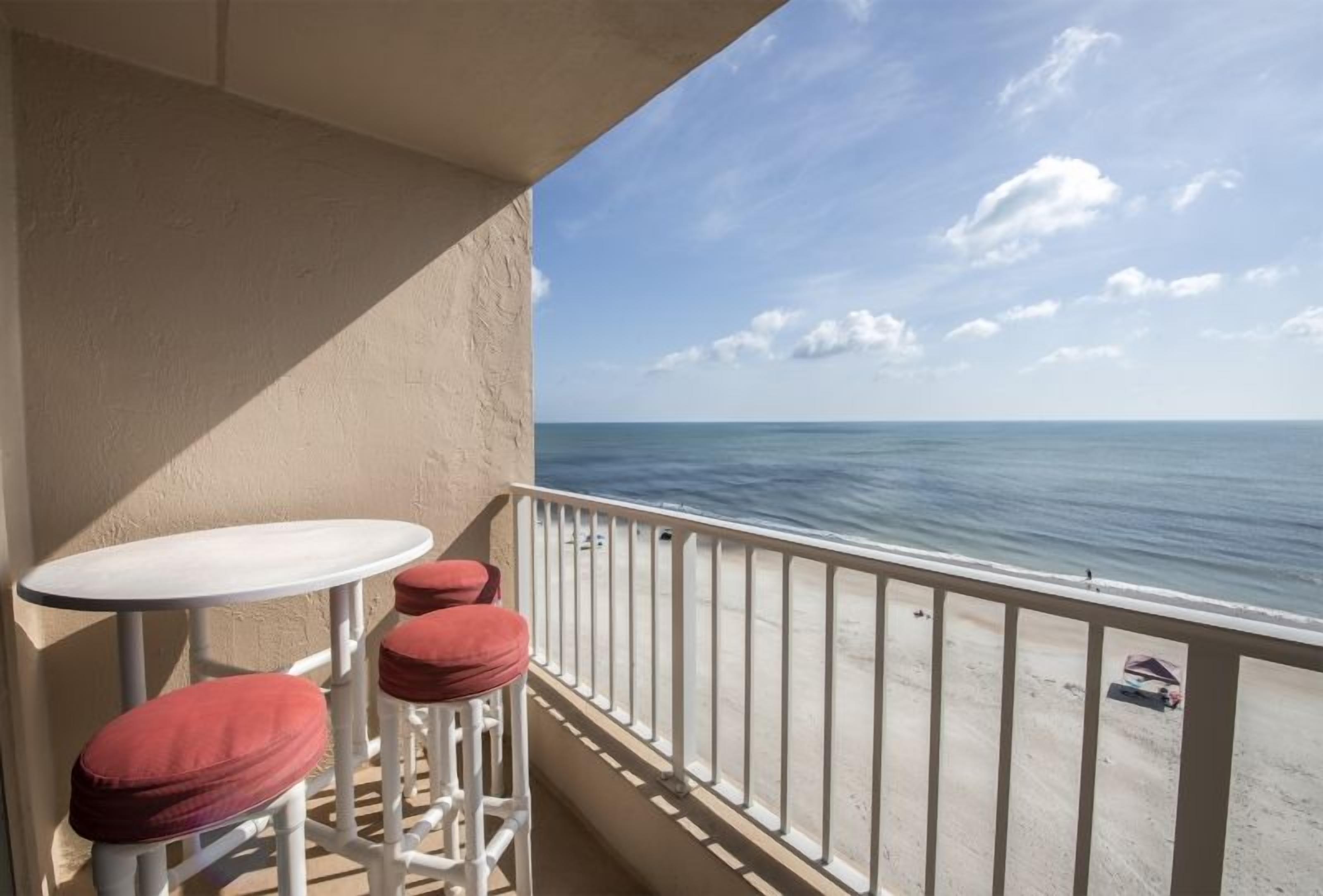 A balcony with a white railing, a small round table, and two red cushioned stools.