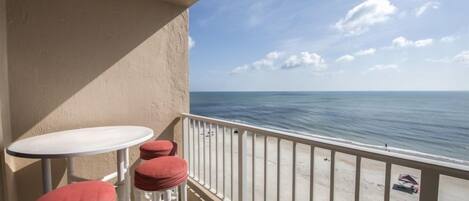 A balcony with a white railing, a small round table, and two red cushioned stools.