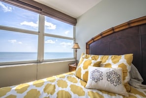 A bed with a patterned bedspread, a window with a view of the sea, and a wooden headboard. - 7th Floor Unit 709 Oceanfront with Great Views in Ponce Inlet (Ponce Inlet)