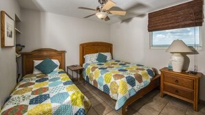 Une chambre avec deux lits, un ventilateur de plafond, une table de chevet avec une lampe et une fenêtre donnant sur un beau paysage.