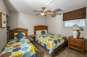 A bedroom with two beds, a ceiling fan, a bedside table with a lamp, and a window with a view. - 7th Floor Unit 709 Oceanfront with Great Views in Ponce Inlet (Ponce Inlet)