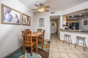 A dining area with a wooden table and chairs, a ceiling fan, and artwork on the walls. - 7th Floor Unit 709 Oceanfront with Great Views in Ponce Inlet (Ponce Inlet)