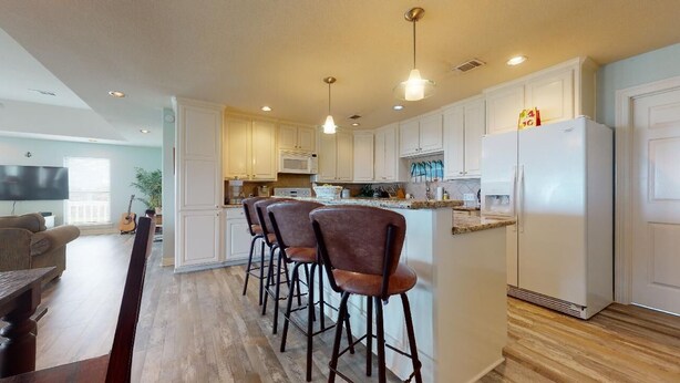 A modern kitchen with white cabinets, a central island with bar stools, a refrigerator, and a microwave. - A Wave From Everything (Bolivar Peninsula)