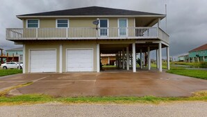 A two-story house with a balcony, two garage doors, and a covered porch. - A Wave From Everything (Bolivar Peninsula)