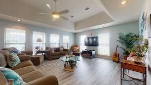 A spacious living room with a ceiling fan, large windows, a flat-screen TV, and a guitar. - A Wave From Everything (Bolivar Peninsula)