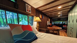 Une pièce confortable avec un lit, une table et une chaise. Il y a des fenêtres donnant sur des arbres.