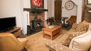 A cozy living room with a fireplace, a television, a sofa, and a coffee table. - Ascot Cottage (York)