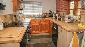 A kitchen with a central island, wooden cabinets, a built-in oven, and a stone backsplash. - Ascot Cottage (York)