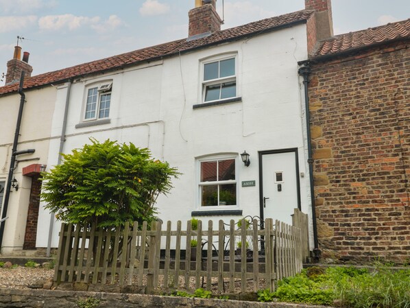 A white building with a brick extension, a wooden fence, and a sign reading "ASCOT".