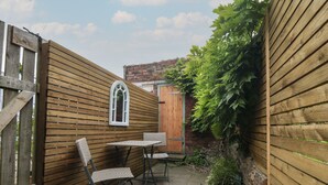 A wooden fence with a window and a door, a small outdoor table with chairs, and a brick wall in the background. - Ascot Cottage (York)