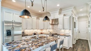Une cuisine moderne avec des meubles blancs, un îlot en marbre, des appareils en acier inoxydable et des luminaires suspendus.