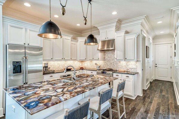 Une cuisine moderne avec des meubles blancs, un îlot en marbre, des appareils en acier inoxydable et des luminaires suspendus.