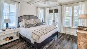 Une chambre à coucher avec un grand lit, un ventilateur de plafond et plusieurs fenêtres équipées de rideaux.