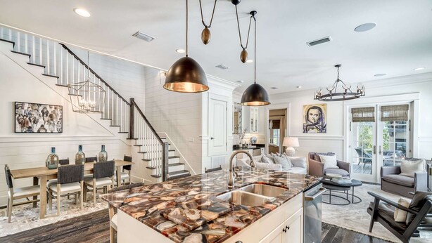 Une cuisine spacieuse dotée d’un îlot central, un coin repas avec une table et des chaises en bois, un escalier et un salon avec un canapé et des fauteuils.