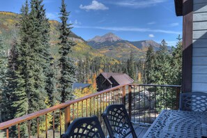 A wooden cabin with a balcony overlooking a forested mountain landscape.