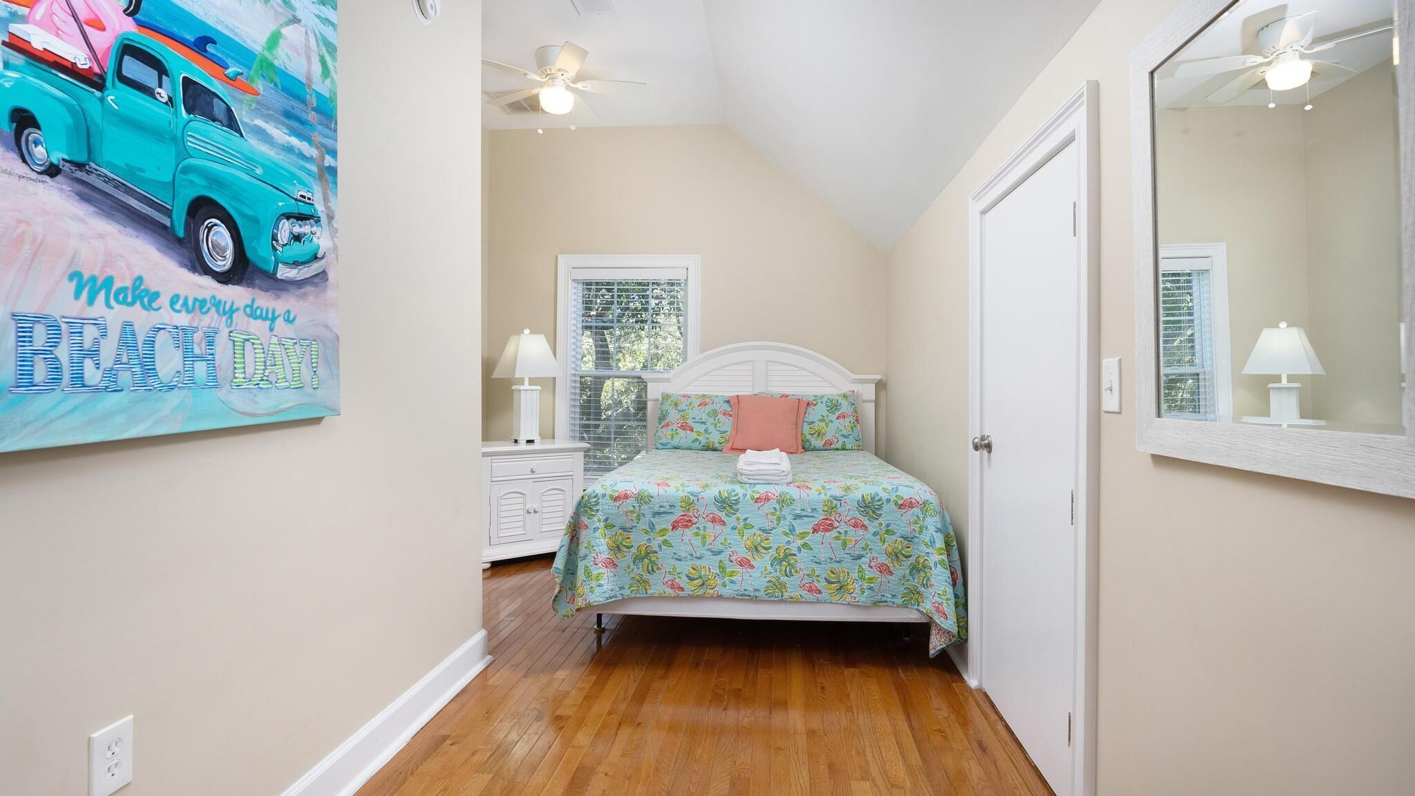 A bedroom with a bed, a ceiling fan, a window with blinds, and a wall with a beach-themed poster.