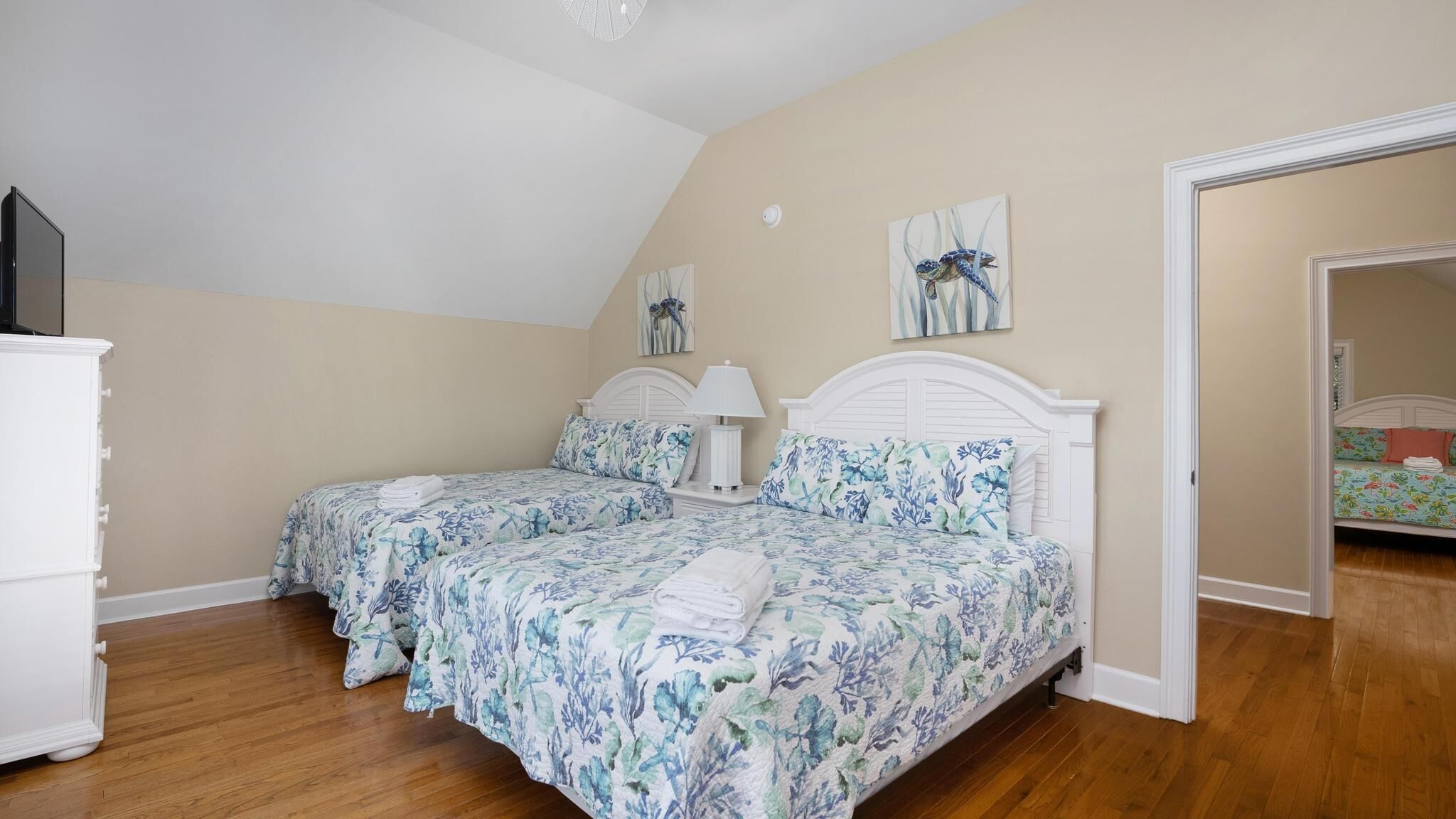 A bedroom with two beds, a white dresser, and a ceiling fan.