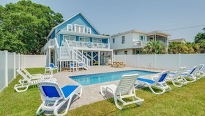 Une maison à deux étages avec une piscine, des chaises longues blanches et un espace couvert sur lequel est affiché un panneau indiquant : « Blue Moon Beach House ».