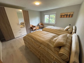 A bedroom with two beds, a wardrobe, a window, and a chair.
