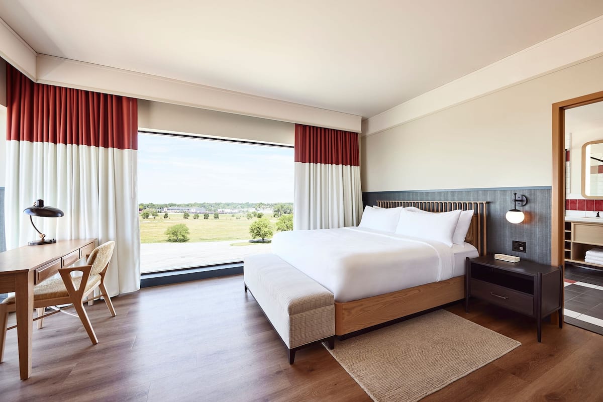 A hotel room with a large bed, a desk with a chair, a nightstand, and a view of the outdoors.