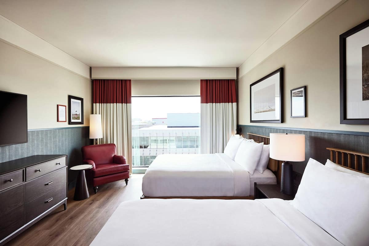 A hotel room with a large bed, a red armchair, a desk with a lamp, and a TV.