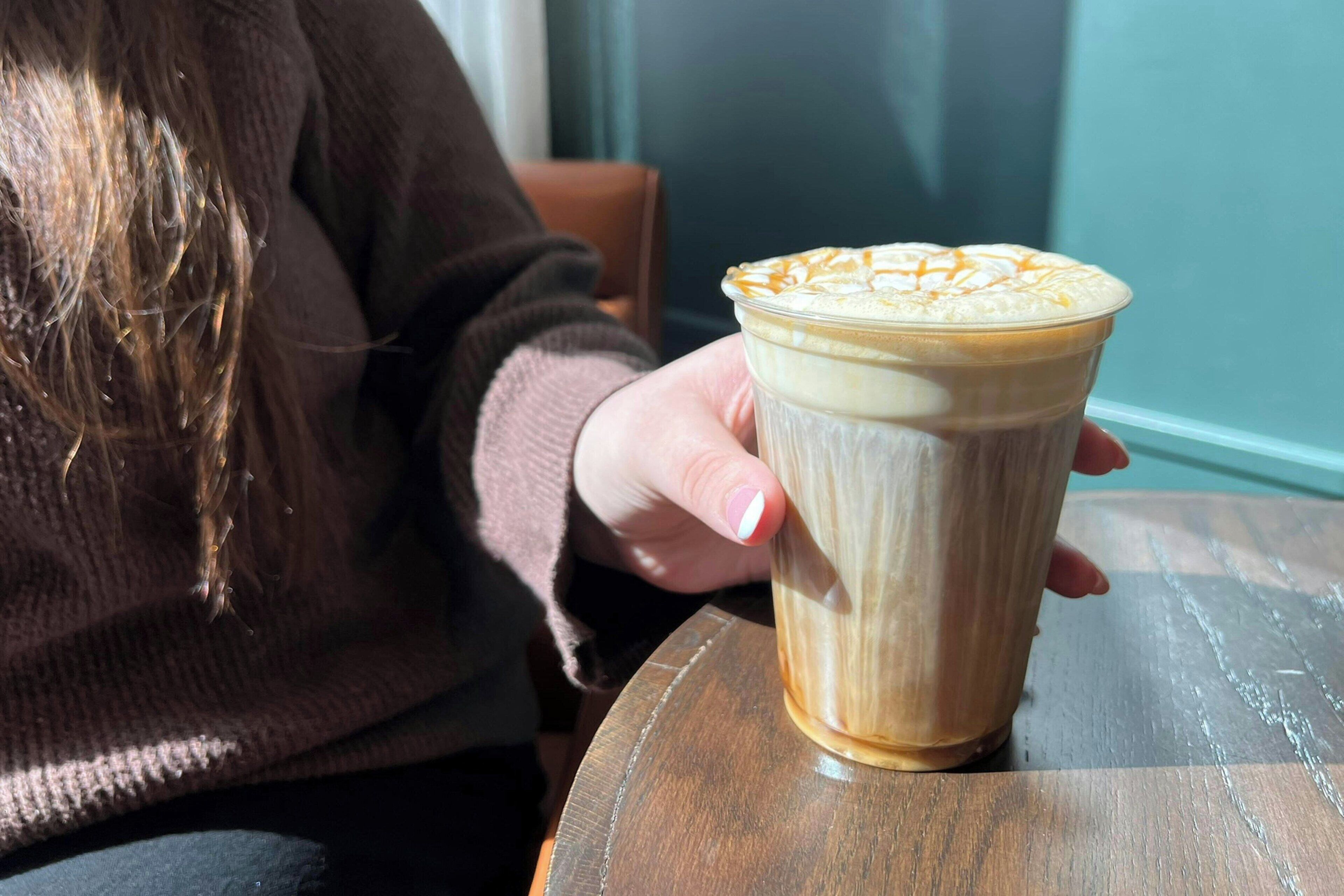 Una persona sosteniendo una taza de café con arte de latte sobre una mesa de madera.